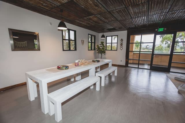 Dining area with long white tables and benches beside glass doors